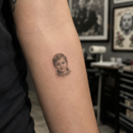 Realistic microrealism tattoo on forearm showing a tiny detailed portrait with fine shading in a professional tattoo studio